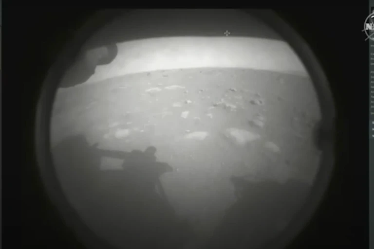 Dusty, black and white image showing martian surface and shadow of Perseverance