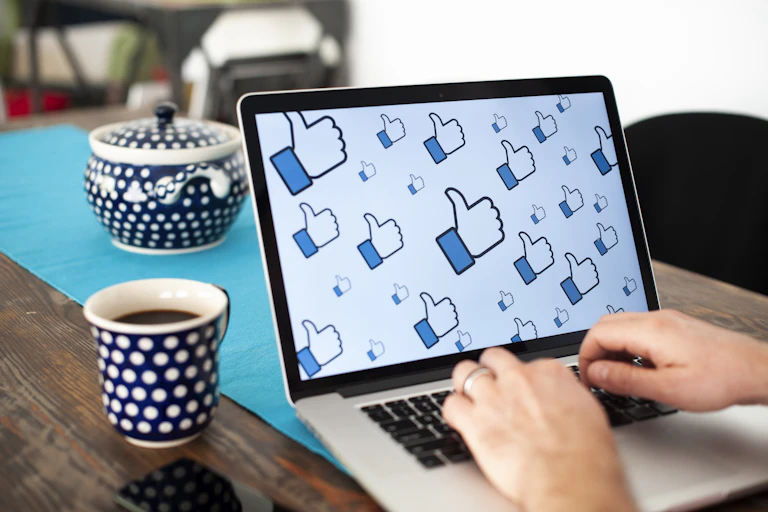 A laptop on a table, a person's hands on the laptop's keyboard, and several dozen social media "like" icons on the otherwise blank laptop screen