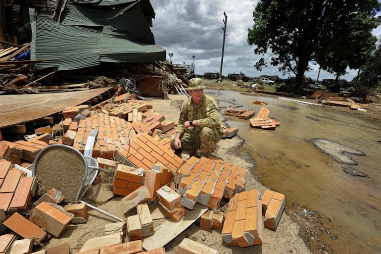 Soldier crouches among the rubble of a house destroyed by flooding