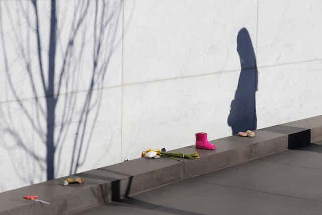 Personal items and a woman's shadow next to Christchurch earthquake memorial wall