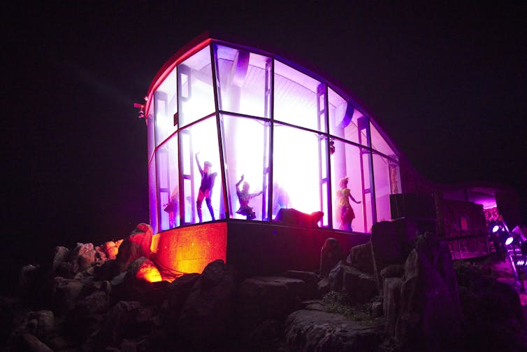 Performers inside pink light-filled enclosed stage