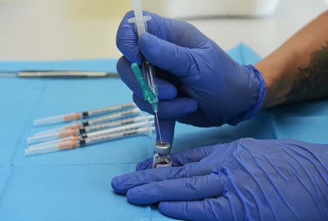 Gloved hands putting syringe into vaccine vial