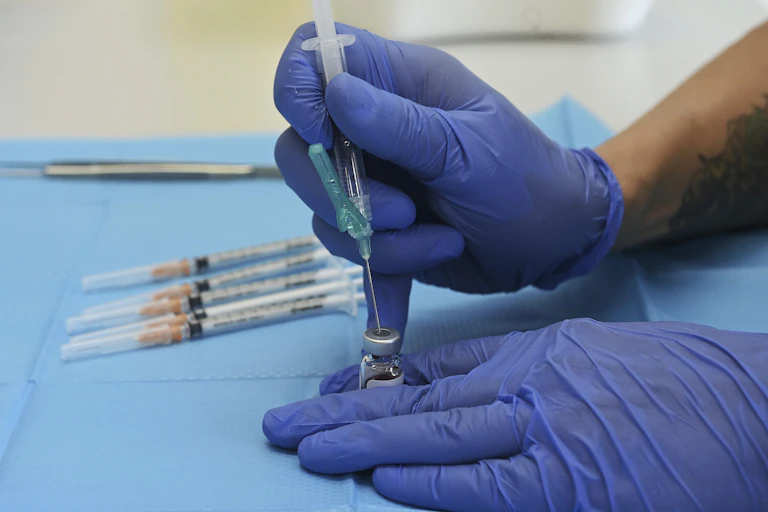 Gloved hands putting syringe into vaccine vial