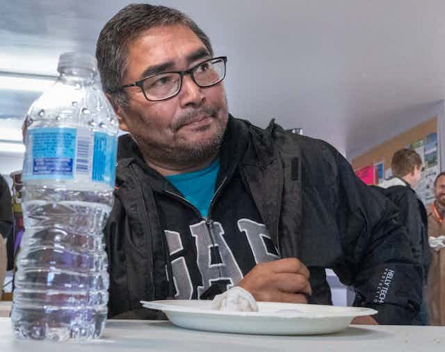 Chief Rudy Turtle sitting at a table with a water bottle and an empty plate in the foreground.
