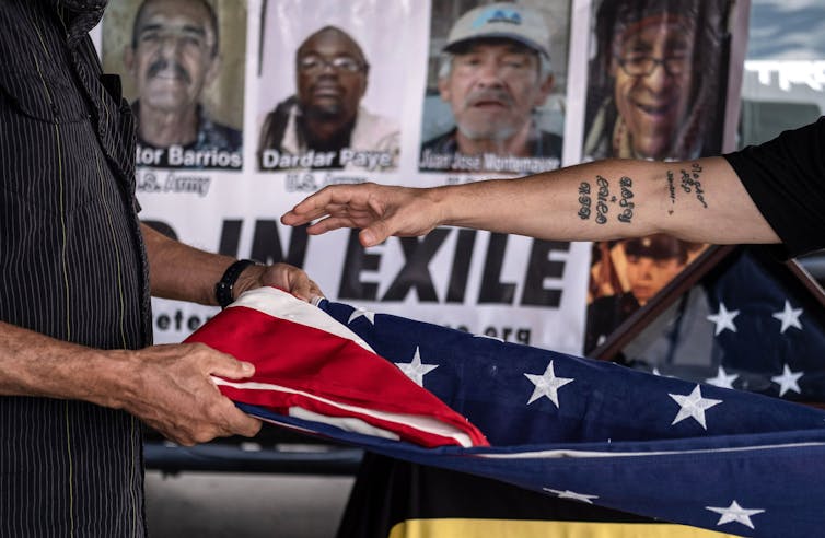 Arms fold an American flag; in background, pictures of 'veterans in exile'