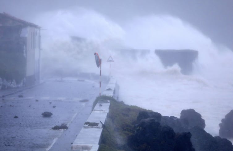 Waves crashing over a seafront road covered in debris.