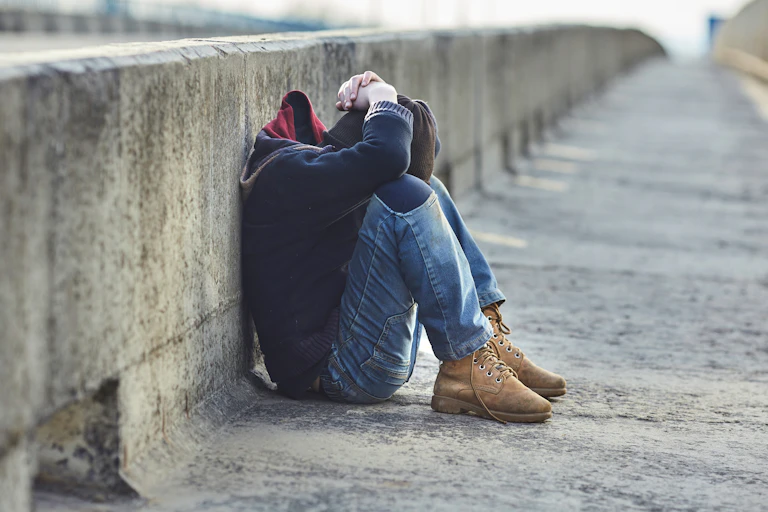A young person sitting on the ground with their head on their knees