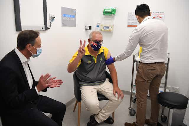 Scott Morrison receives the pfizer vaccine, while giving a "V" sign