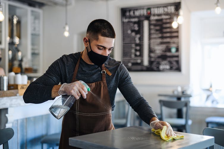 A young man, cleaning tables at a coffee shop.