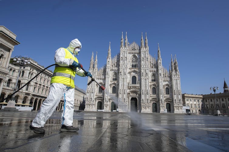 Cleaner in hazmat suit disinfecting the pavement in Duomo square, Milan, Italy.