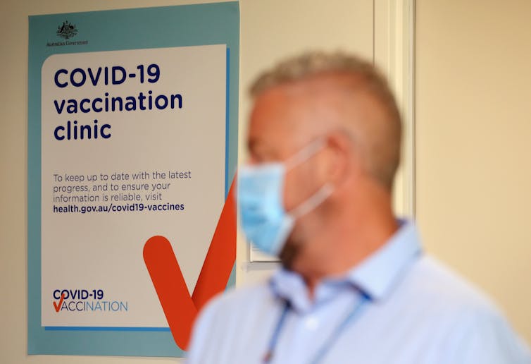 A man wearing a mask walks past a sign saying 'COVID-19 vaccination clinic'.