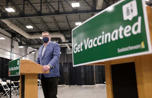 Saskatchewan Premier Scott Moe stands at a podium with a sign reading "Get Vaccinated" in the foreground