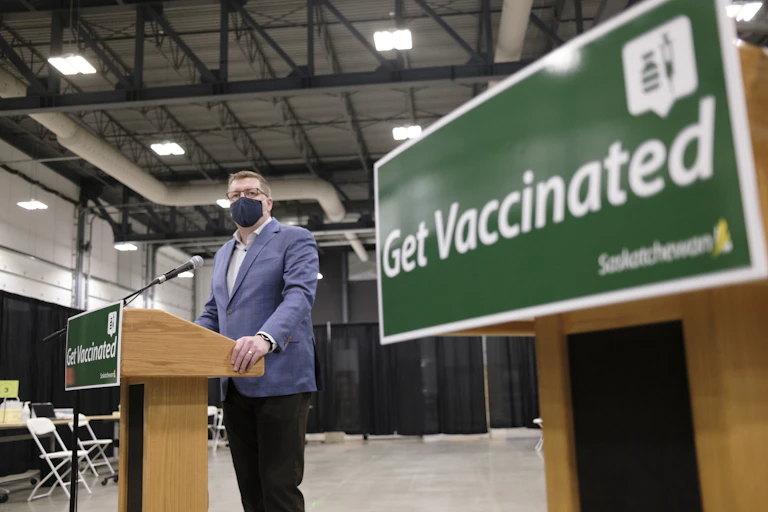 Saskatchewan Premier Scott Moe stands at a podium with a sign reading "Get Vaccinated" in the foreground