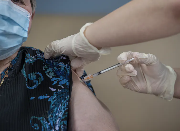 Close-up of a woman's shoulder being injected by a health-care worker out of frame