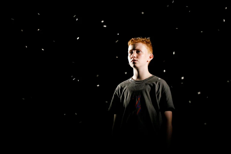 A boy stands surrounded by black