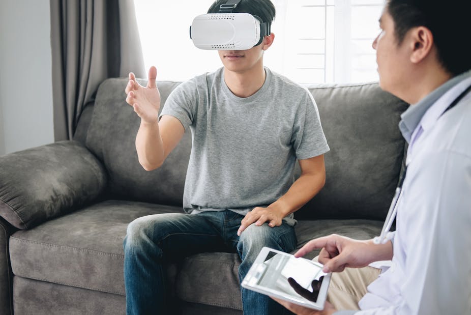 Man wearing virtual reality headset is monitored by his therapist.