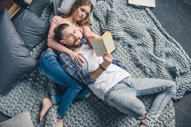 Man laying on woman's chest on the floor on top of a blanket while reading to her