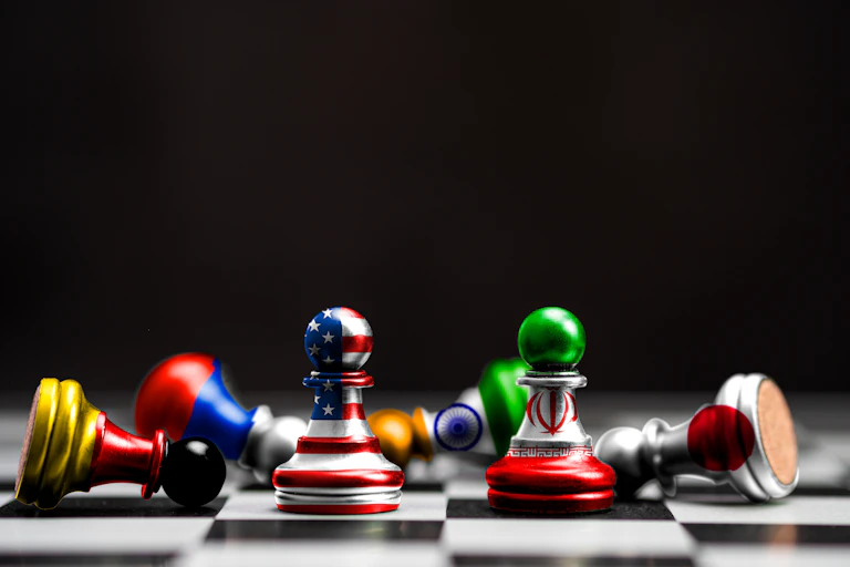 Chessboard with pawns in the colours of USA and Iran with pieces representing other countries knocked over.