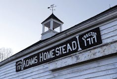 A sign on a white clapboard carriage house reads Adams Homestead, Erected 1717