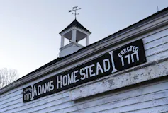 Une pancarte sur une remise à claques blanche indique Adams Homestead, Erected 1717