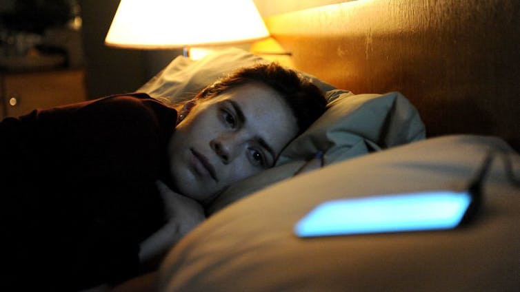 A woman lying in bed looking at a lit-up phone screen on a pillow