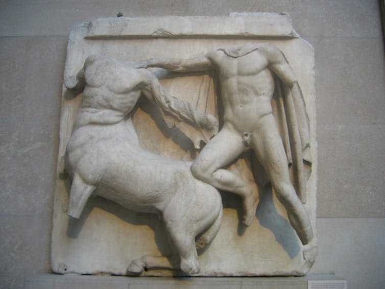 A white marble sculpture of two headless male figures with muscular torsos.