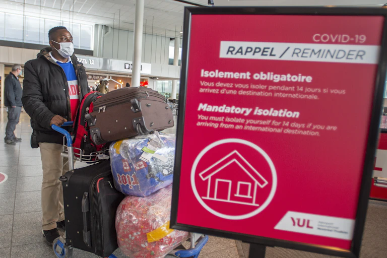 Masked passenger at airport walks past sign reminding about quarantine requirements
