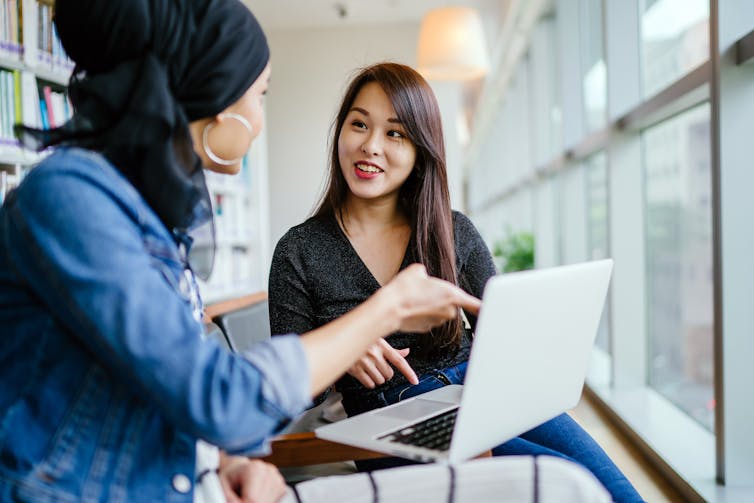 Two women chat while looking at a computer.