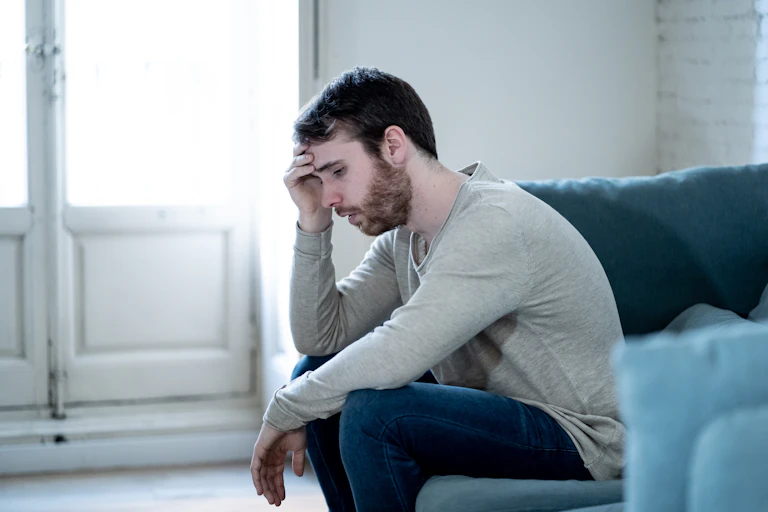 A young man sits on a couch looking sad.