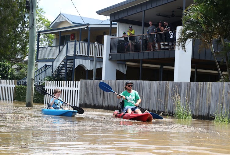 Man and child kayak down flooded street