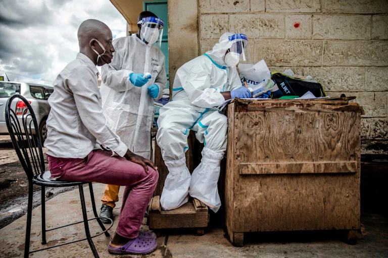 Health workers wearing personal protective equipment (PPE) collect data from a man before taking samples
