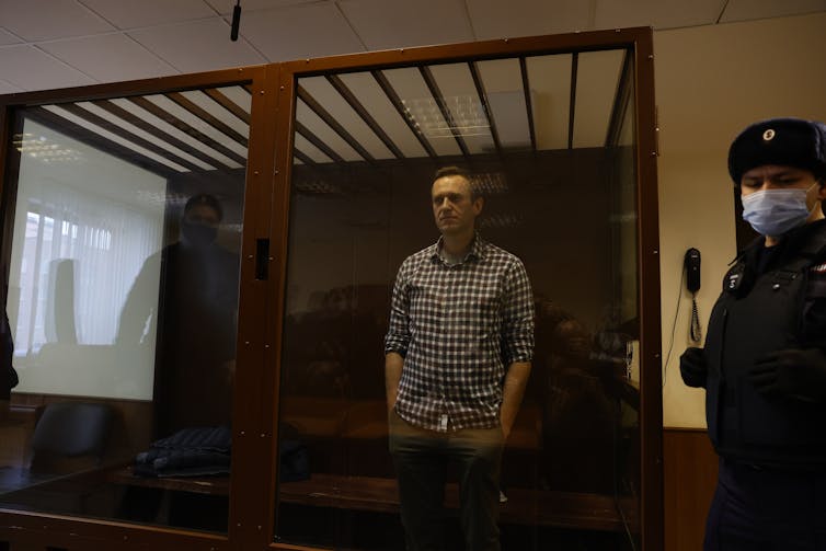 Alexei Navalny standing in court in a glass cell.