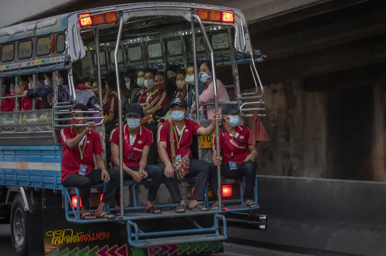 Crowded masked workers wearing the same red shirts look out from a bus window.