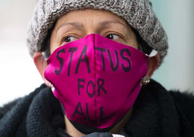 A woman wears a pink mask which says, "Status for all."