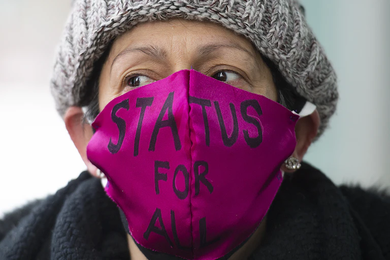 A woman wears a pink mask which says, "Status for all."