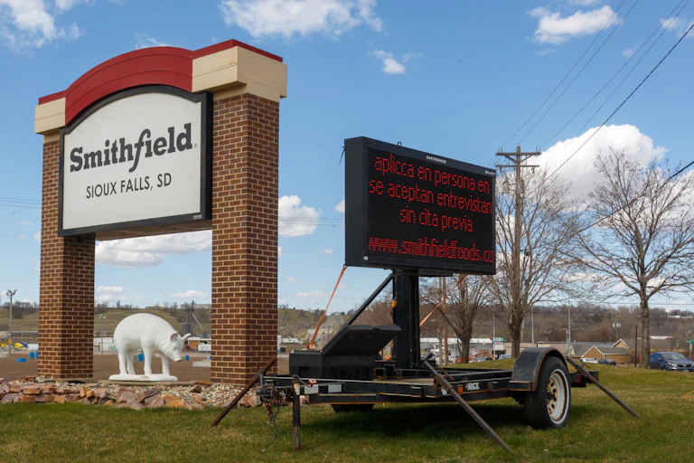 Entry sign with billboard advertising jobs in Spanish.