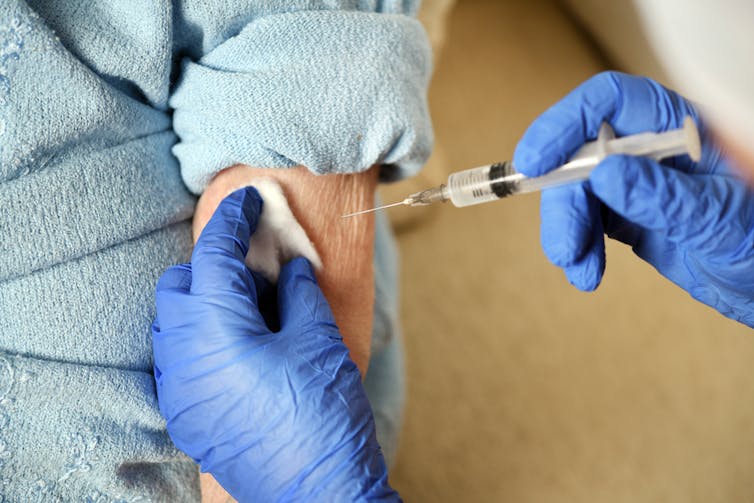 Elderly person getting vaccinated by health worker wearing gloves