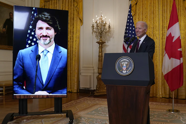 Biden stands behind a podium as Trudeau smiles on a screen.