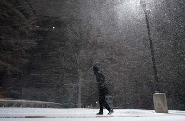 A person dressed in black walks through a blizzard at night 