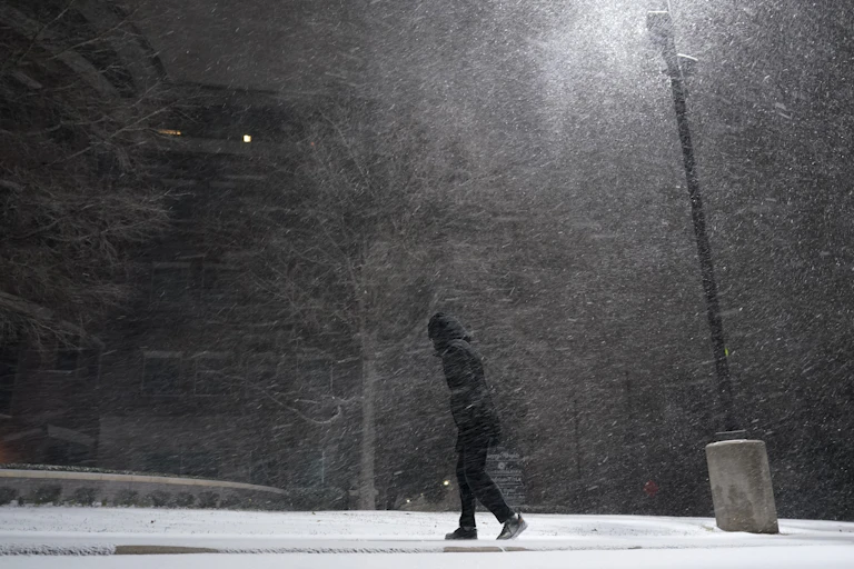 A person dressed in black walks through a blizzard at night