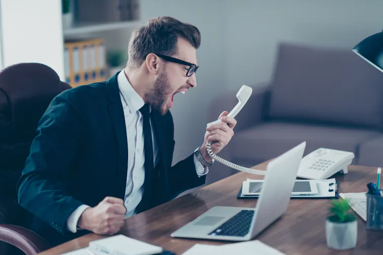 A man at a desk shouting into a phone.