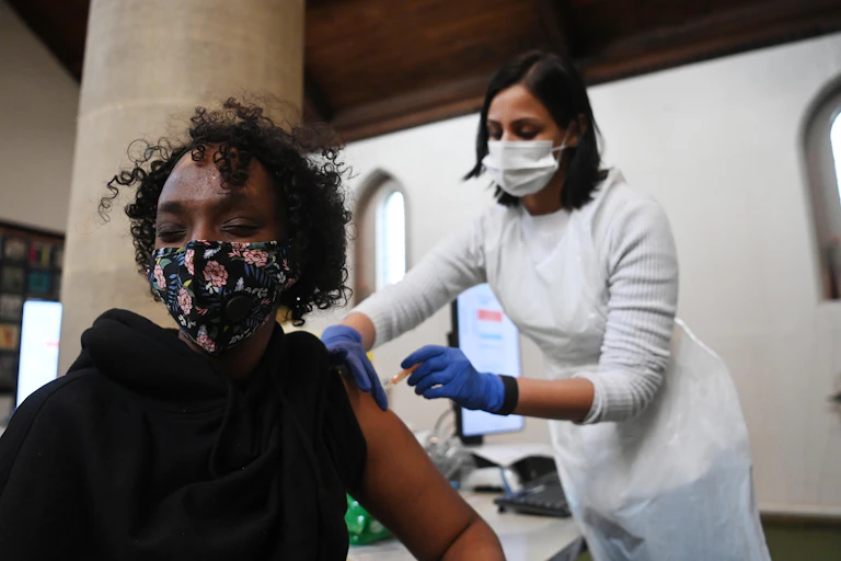 Woman in black top and face mask closes eyes while receiving the AstraZeneca COVID-19 vaccine