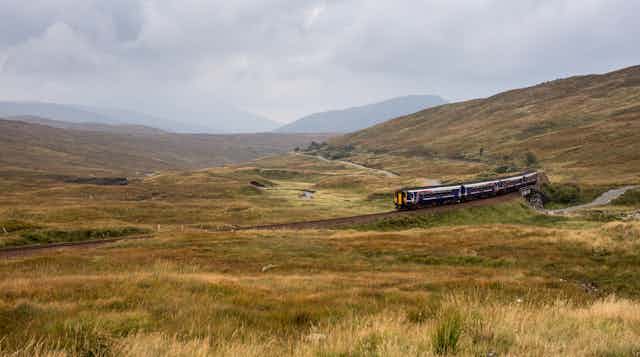 A three-carriage ScotRail train trundling across a bleak Rannoch Moor in the Highlands.