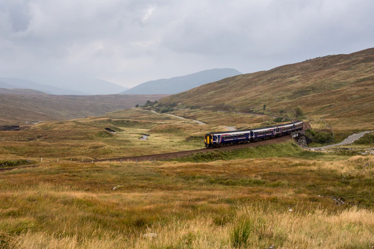 A three-carriage ScotRail train trundling across a bleak Rannoch Moor in the Highlands.