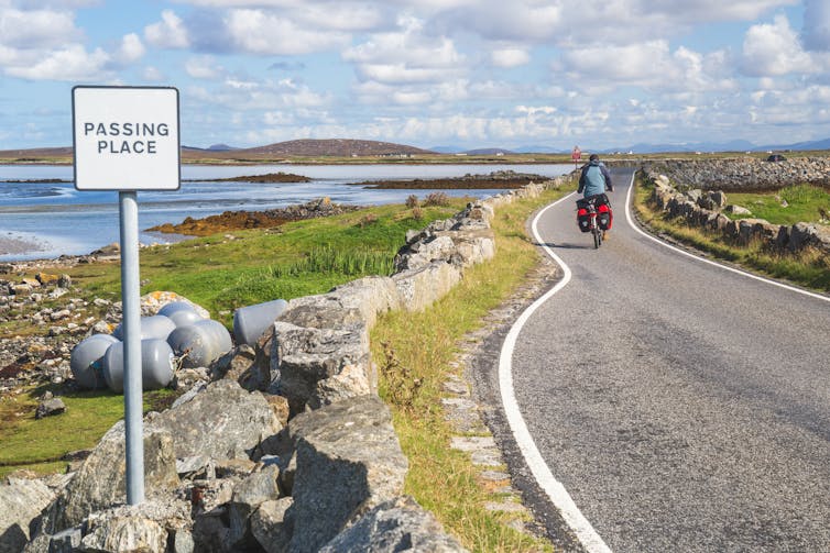 A cyclist crossing one of the causeways on Uist on a blue-sky sunny day.