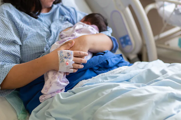A woman cradles a newbord baby in hospital.