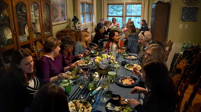 Large group of women converse and eat a shared meal at two dining room tables.