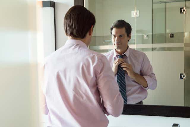 Man adjusting his tie in the mirror.