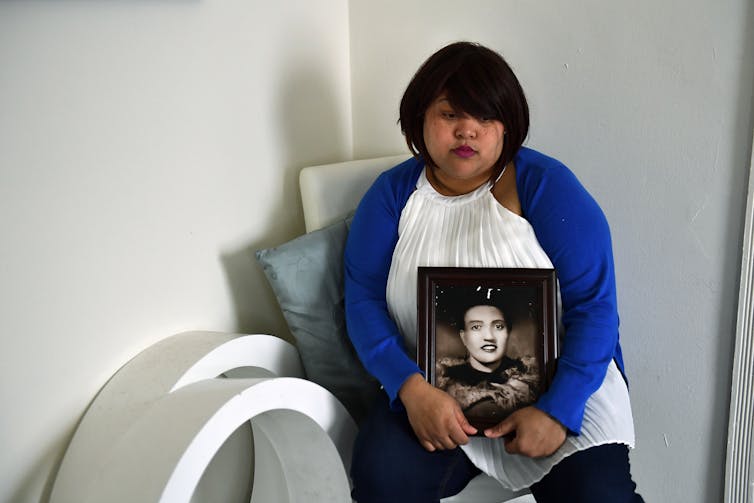 Seated woman holds a black and white photo of a woman