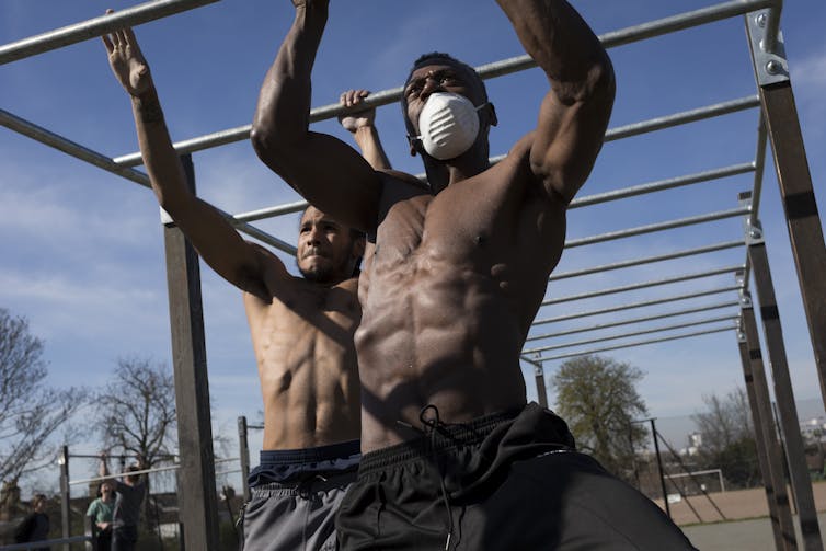 Two men using exercise bars outdoors.